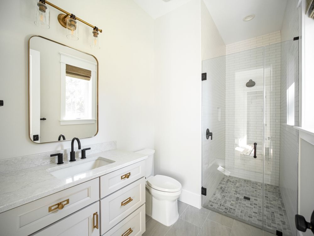 Bright white modern bathroom with vanity, mirror, toilet, and glass walk-in shower.