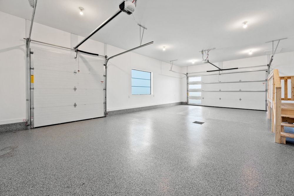 Bright empty garage with gray epoxy floor, white walls, overhead lights, and a small window.