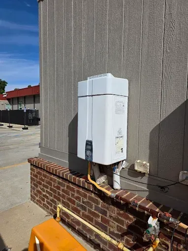 Outdoor tankless water heater on brick and siding exterior wall. Yellow gas pipes visible.