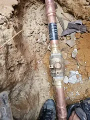 Copper pipes and a brass valve in a dirt trench, likely for water service.