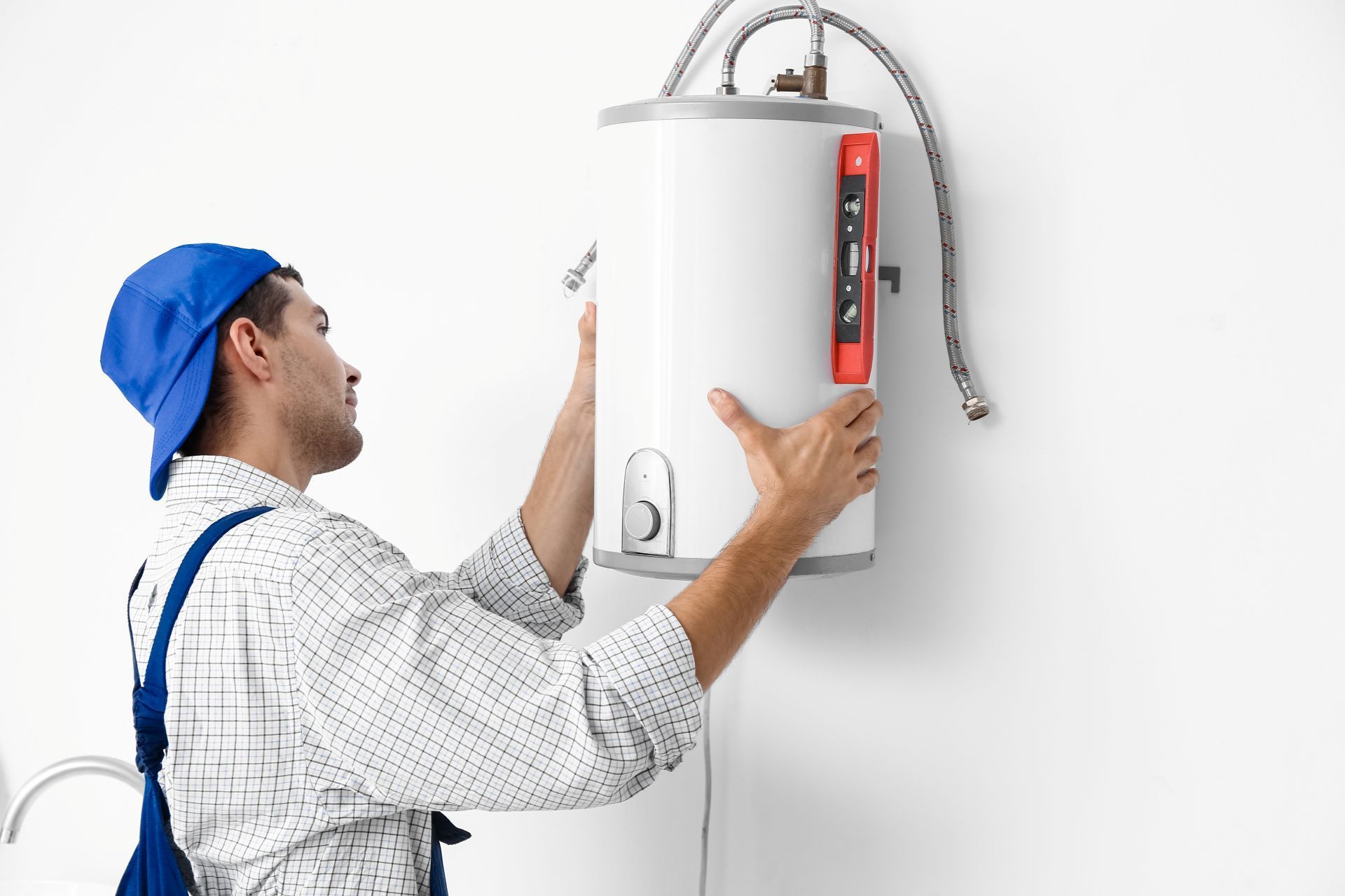 Plumber in blue cap installing a water heater on a white wall.