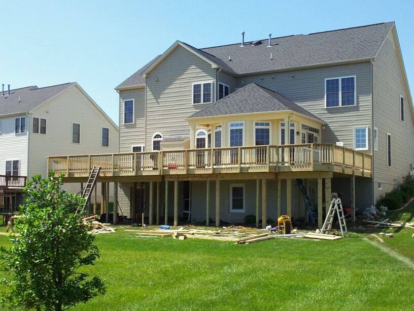 Backyard view of a house with a deck under construction; green grass, blue sky.