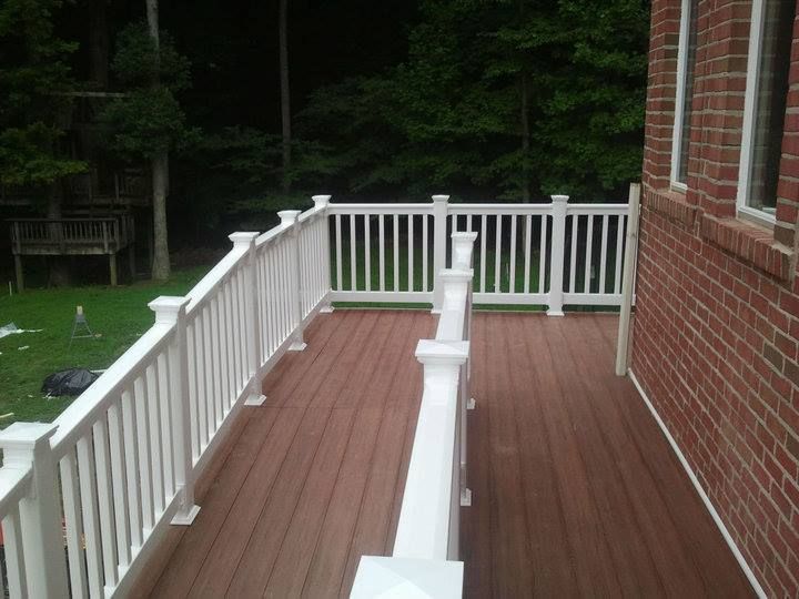 White-railed deck attached to a brick house. Brown deck boards, green yard and trees in the background.
