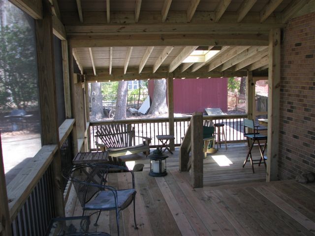 Screened-in wooden porch with seating and a view of a backyard with trees and a red shed.