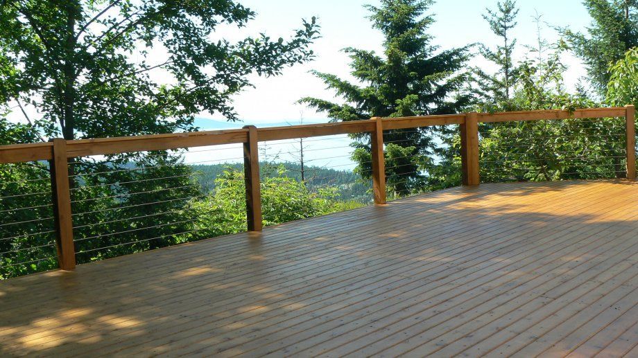 Wooden deck with railing overlooking trees and a body of water under a blue sky.