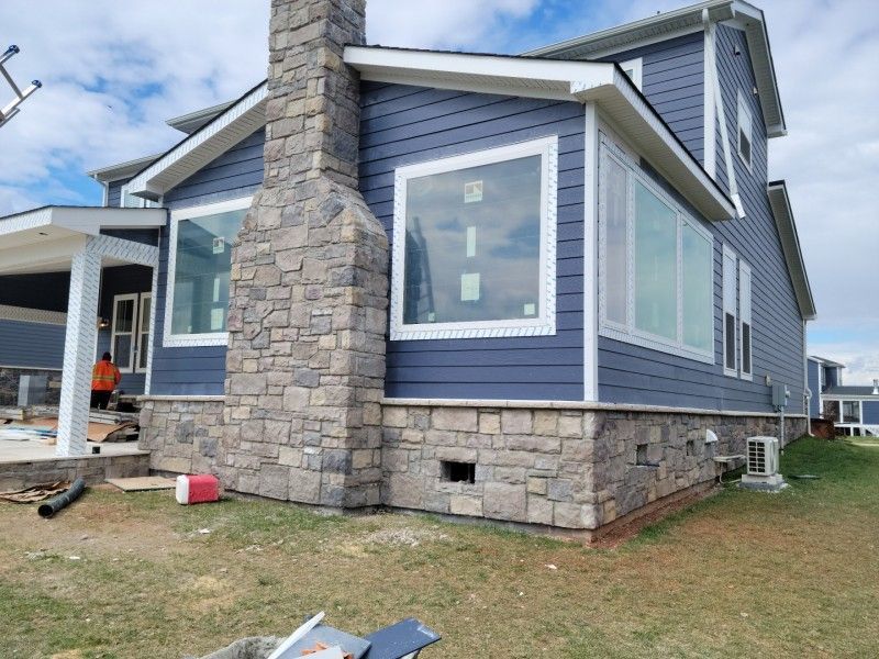 Blue house with stone chimney and base; windows and construction materials visible.