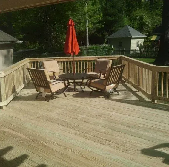 Wooden deck with seating, orange umbrella, and small building in background.