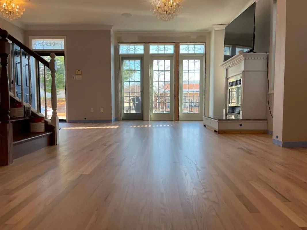 Empty bright living room with hardwood floors, chandeliers, and large French doors opening to a balcony