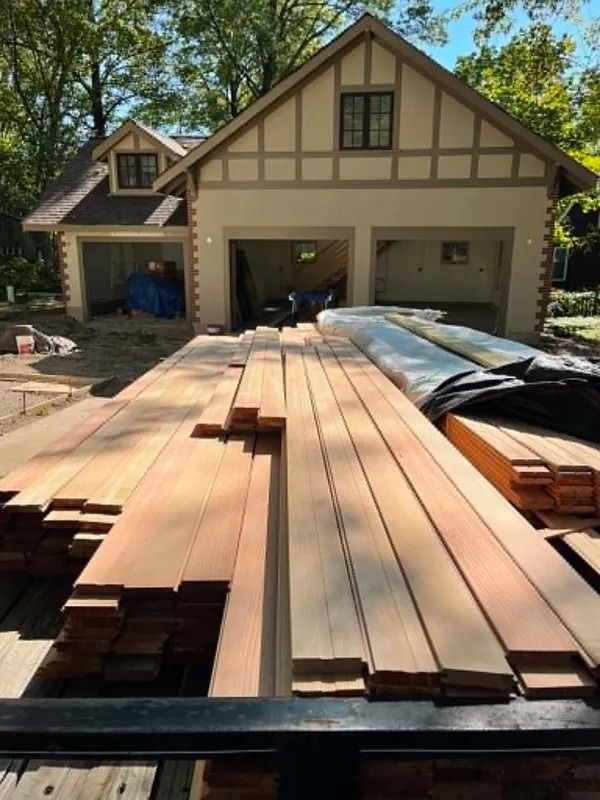 Stacks of lumber laid out in a driveway in front of a house under construction