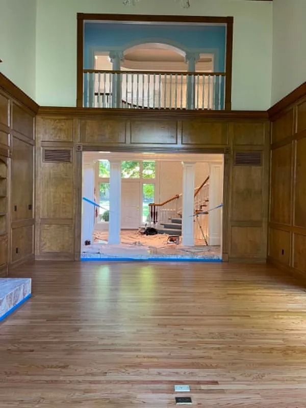 Empty wood-paneled room with hardwood floors and an open doorway to a brighter adjoining space