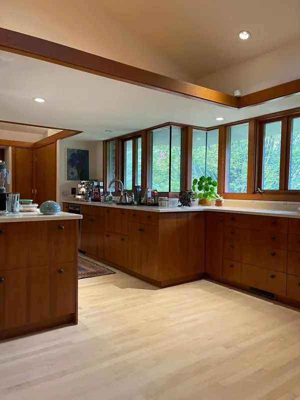 Modern kitchen with wooden cabinetry, large windows, light wood floor, and a central island