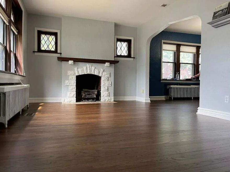 Empty living room with dark wood floors, white fireplace, and blue accent wall.