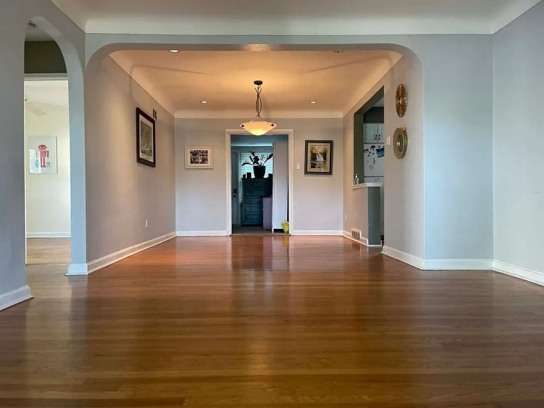 Empty hardwood-floored living room with gray walls and arched openings leading to a hallway.