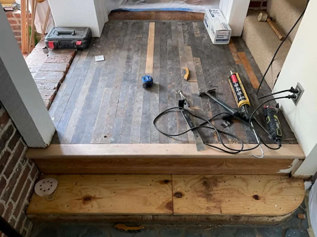 Partially built wooden floor with tools, wires, and a measuring tape in an indoor renovation space