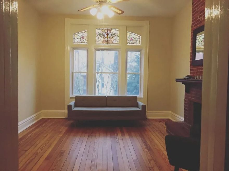 Empty living room with hardwood floors, a bench under a large window, and a ceiling fan.