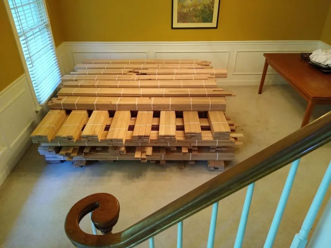 Stacked wooden pallets in a room beside a staircase and small table.