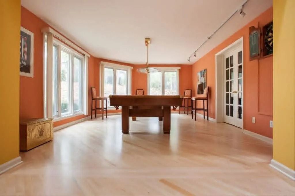 Bright orange game room with a pool table, light wood floor, and large windows