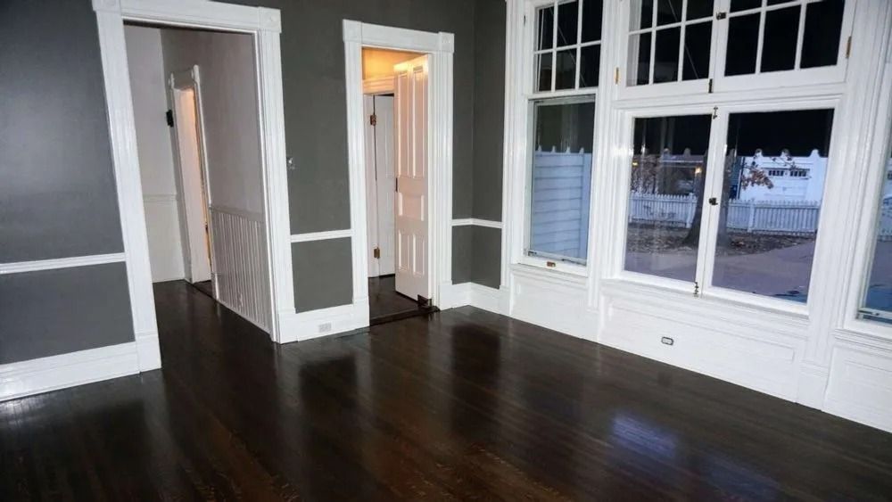 Empty room with dark hardwood floors, gray walls, white trim, and large windows and doorways.