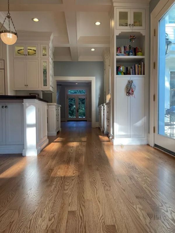 Bright kitchen with white cabinets, hardwood floors, and sunlight streaming through a doorway and windows