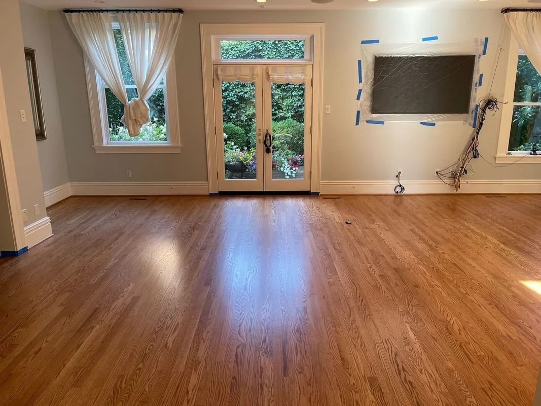 Empty living room with wood floors, large windows, French doors, and a wall-mounted TV area