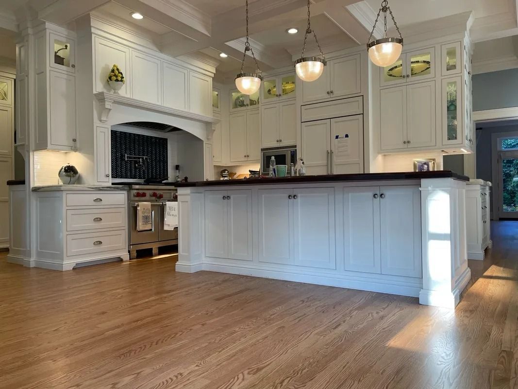 Bright white kitchen with large island, pendant lights, and hardwood floors