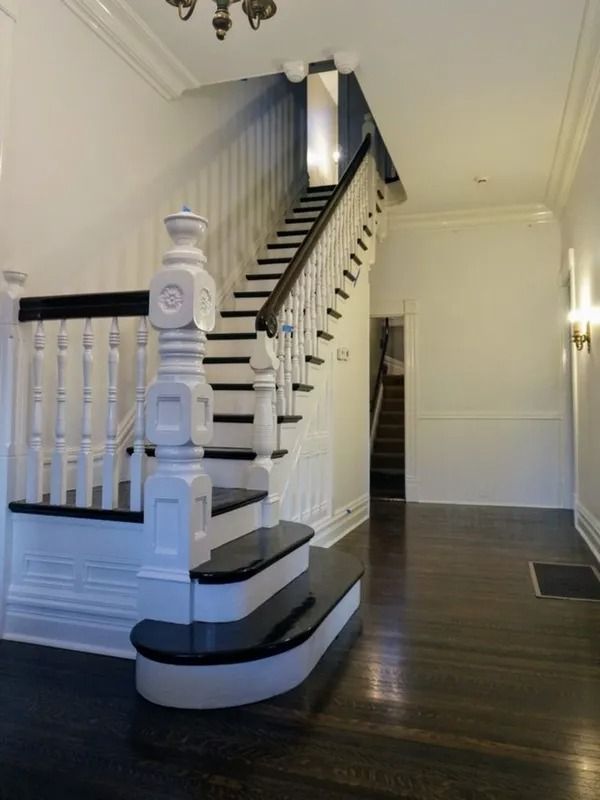 Elegant staircase in a white hallway with dark wood floors and ornate black-and-white railing