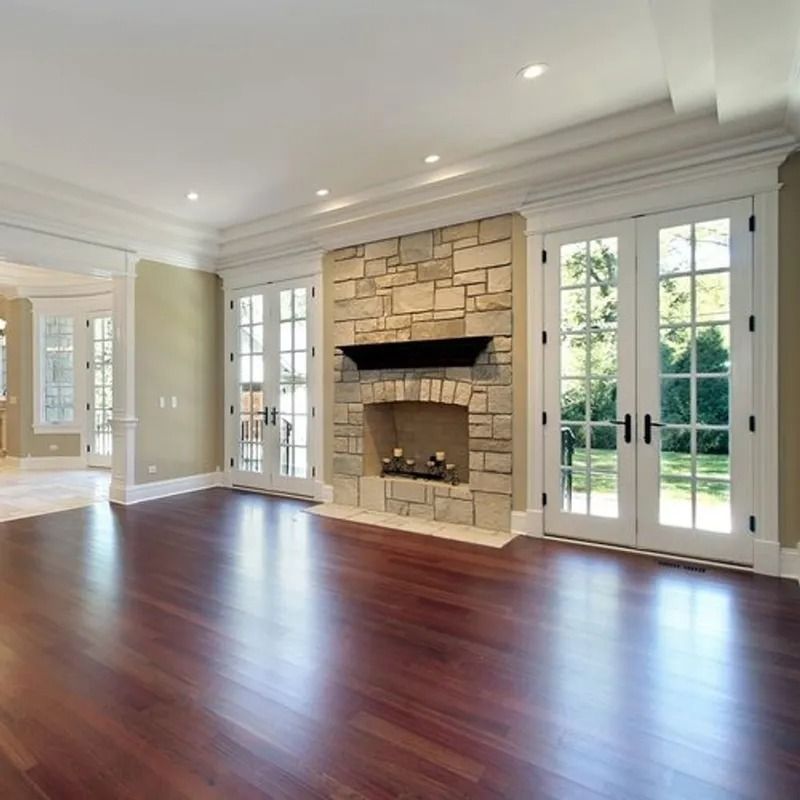 Spacious living room with hardwood floors, stone fireplace, and French doors opening to a bright outdoor view.