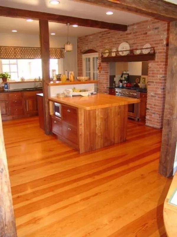 Warm kitchen with polished wood floors, brick fireplace, and wooden island under hanging lights.