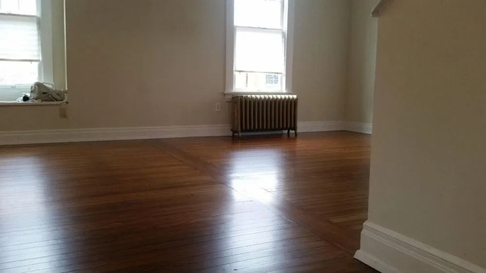 Empty room with hardwood floors, white walls, and two windows above radiators.
