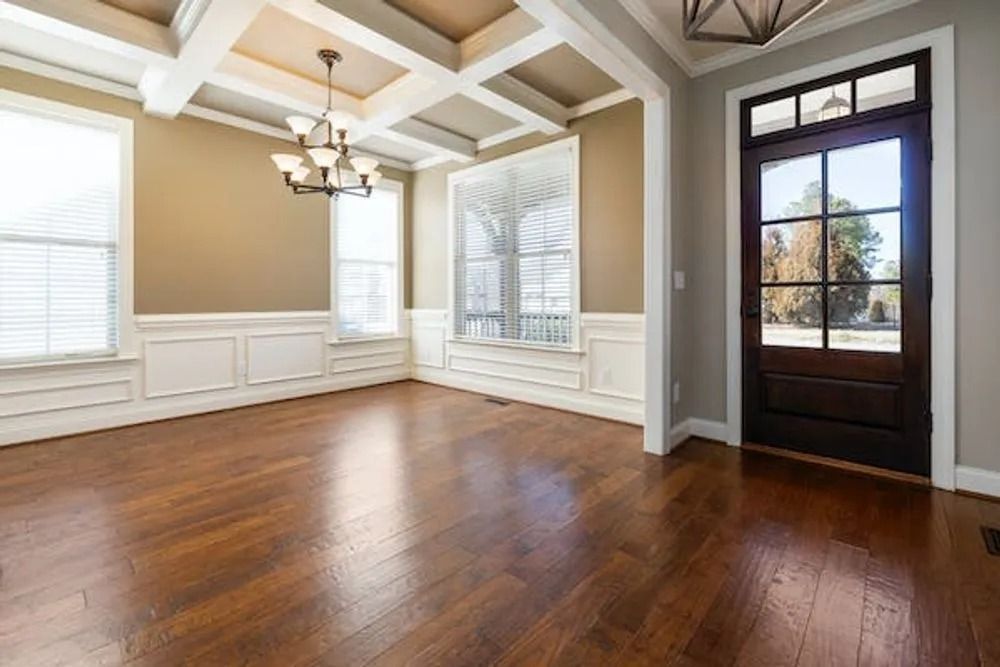Empty living room with hardwood floors, beige walls, white trim, chandelier, and dark front door