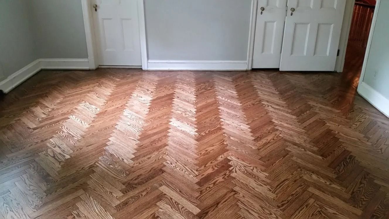 Empty room with herringbone wood floor and white doors, lit by daylight from the left