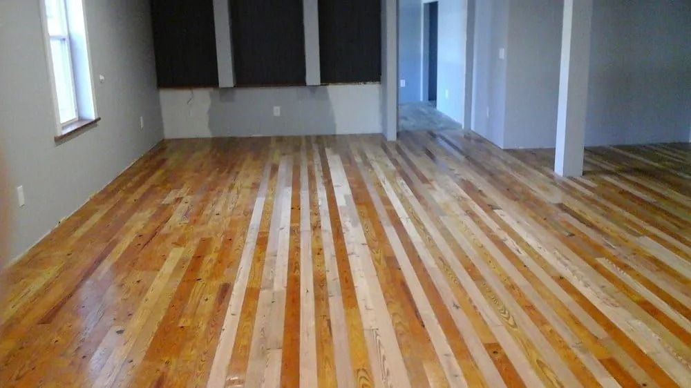Empty room with striped wood floor, white walls, and a window on the left.