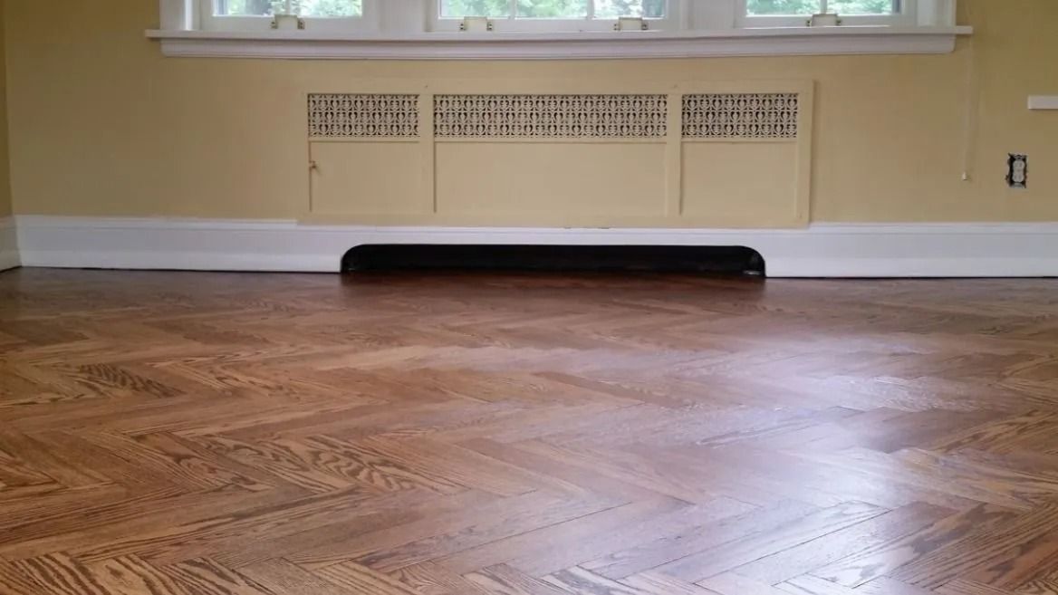 Empty room with hardwood floor, white baseboards, and a vent beneath a window.