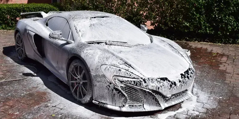 A sports car covered in foam is parked on a sidewalk.