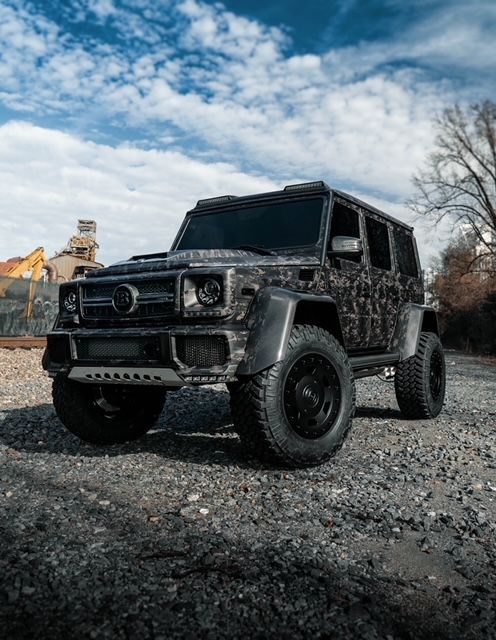 A black mercedes benz g500 is parked on a gravel road.