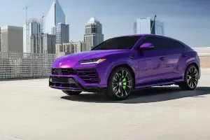 A purple lamborghini urus is parked in a parking lot in front of a city skyline.