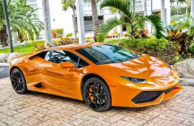 An orange lamborghini huracan is parked on a brick driveway.