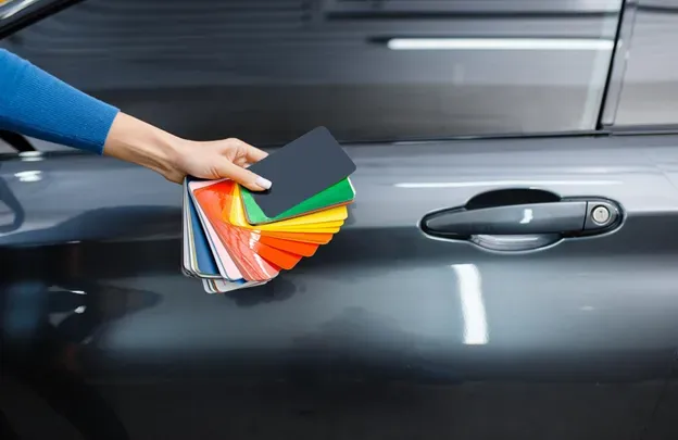 A person is holding a palette of colors in front of a car.