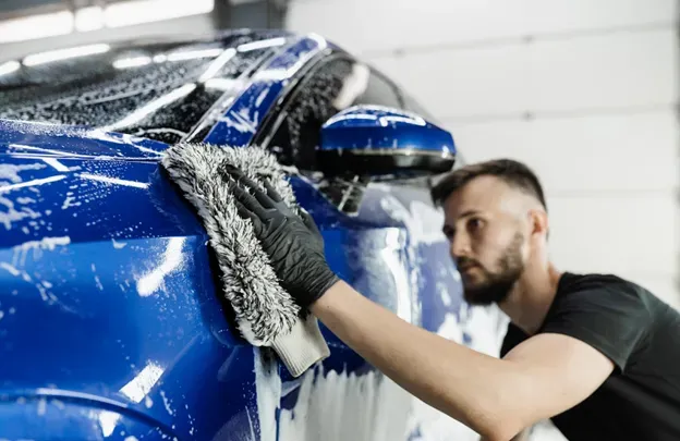 A man is cleaning a blue car with a towel.