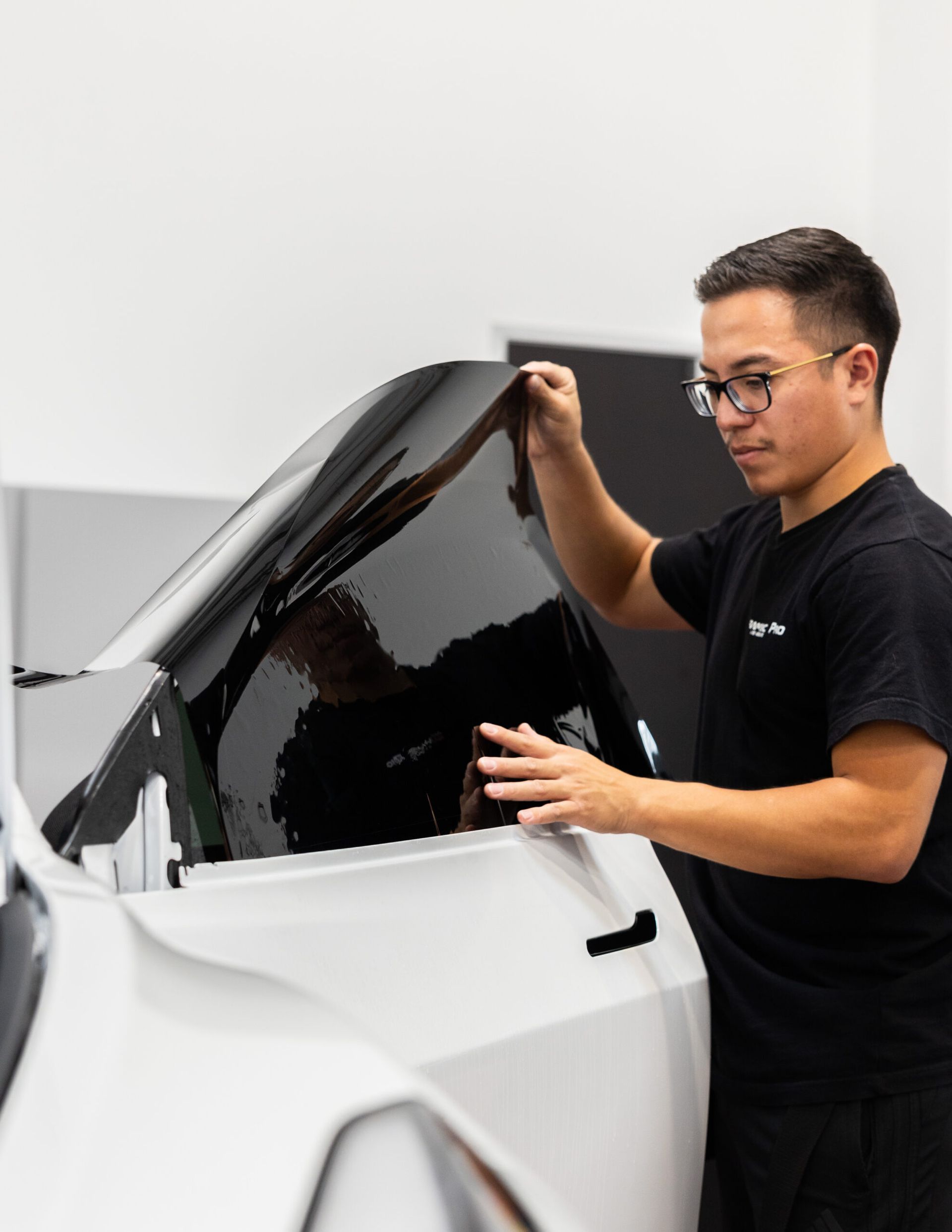 A man is applying window tinting to a white car.
