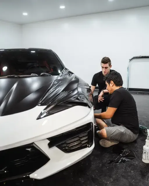 Two men are working on a white sports car in a garage