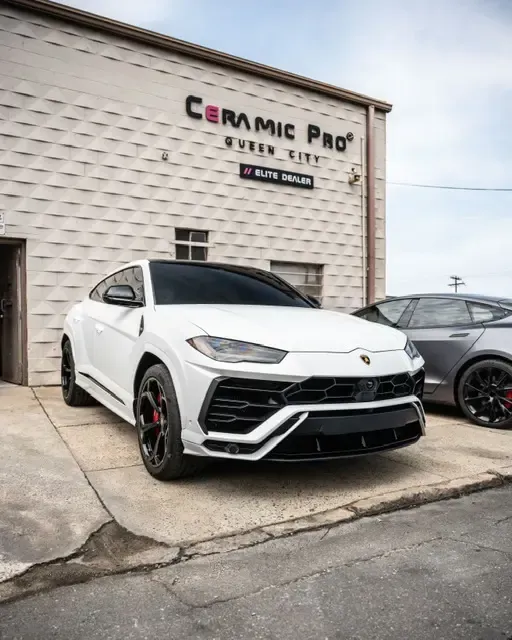 A white lamborghini urus is parked in front of a building.