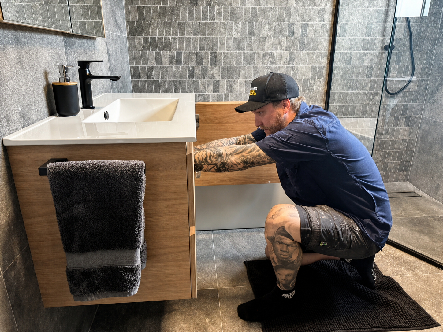 Man Installing a Bathroom Vanity, Crouching Near Open Cabinet — Hot Water Specialist Forster In Forster, NSW