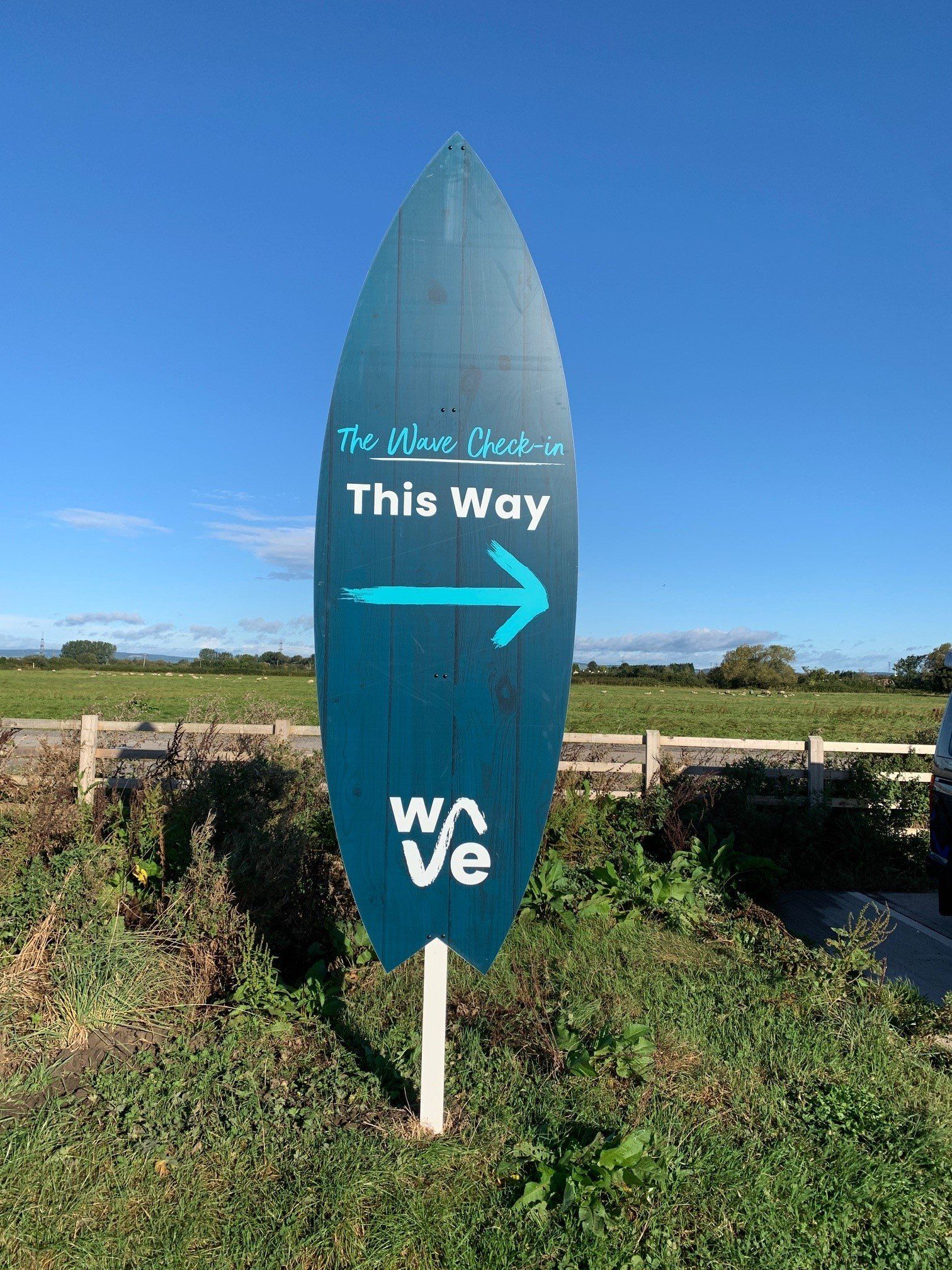A sign in the shape of a surfboard is pointing to the right.