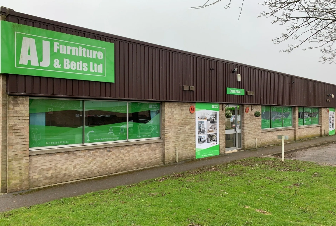 A large brick building with a green sign that says aj furniture & beds ltd.