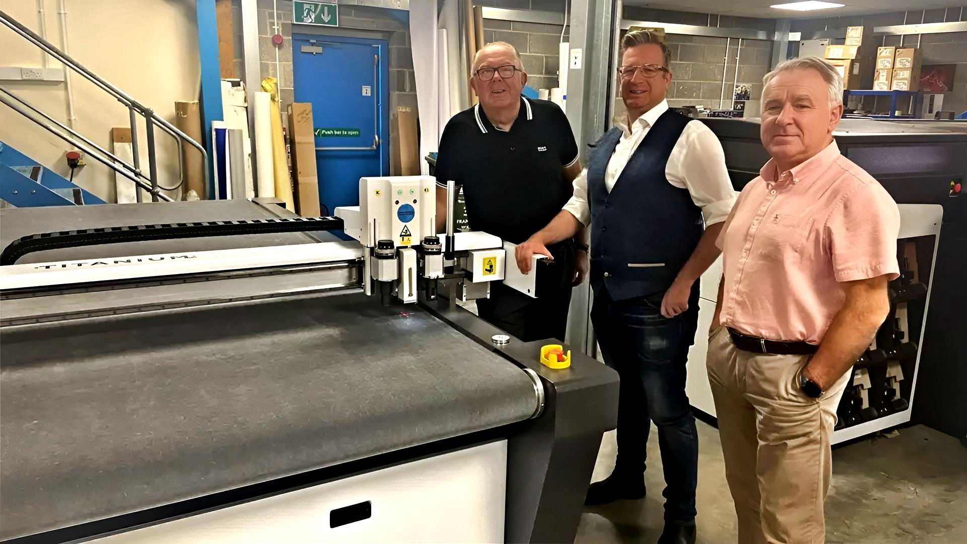 Three men are standing in front of a large printer in a factory.