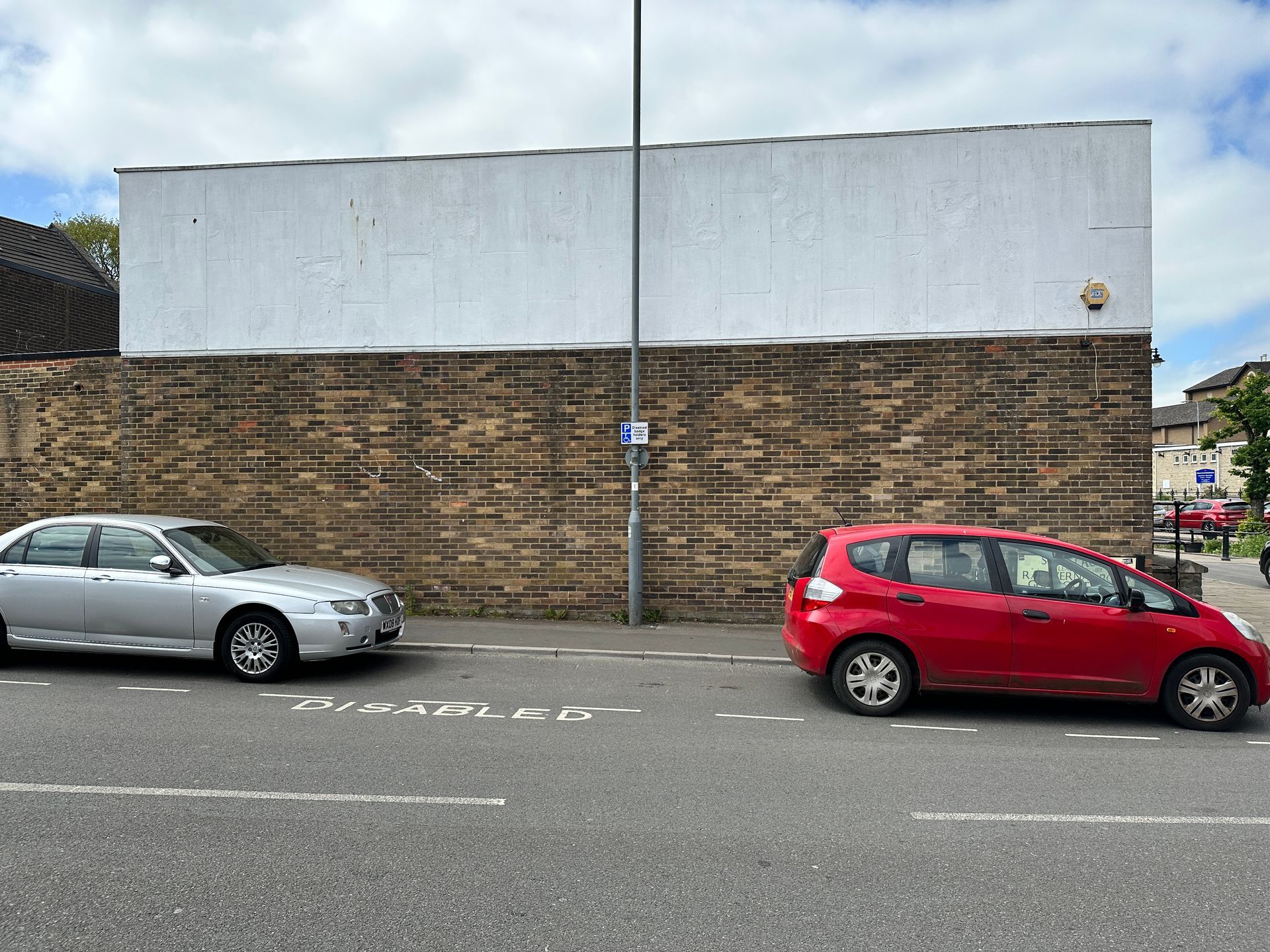 Two cars are parked on the side of the road in front of a brick wall.