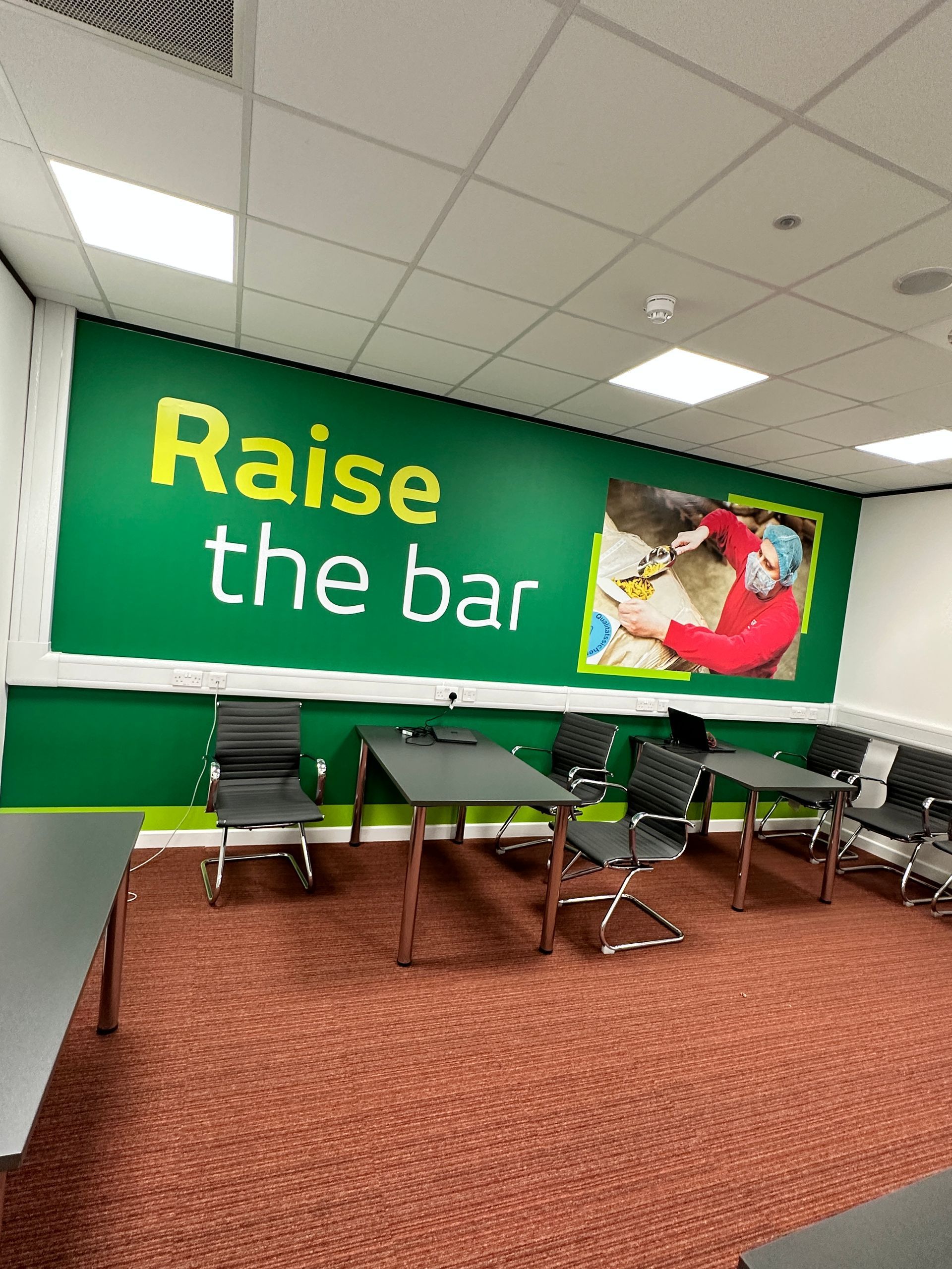 A room with tables and chairs and a sign that says `` raise the bar ''