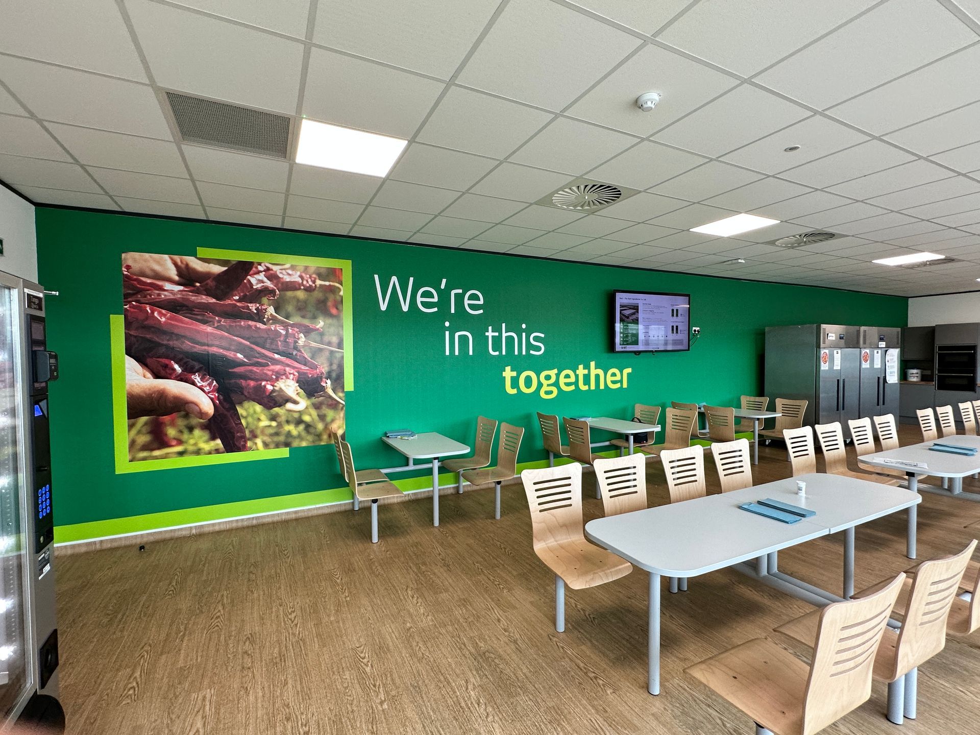 A dining room with tables and chairs and a green wall that says we 're in this together.
