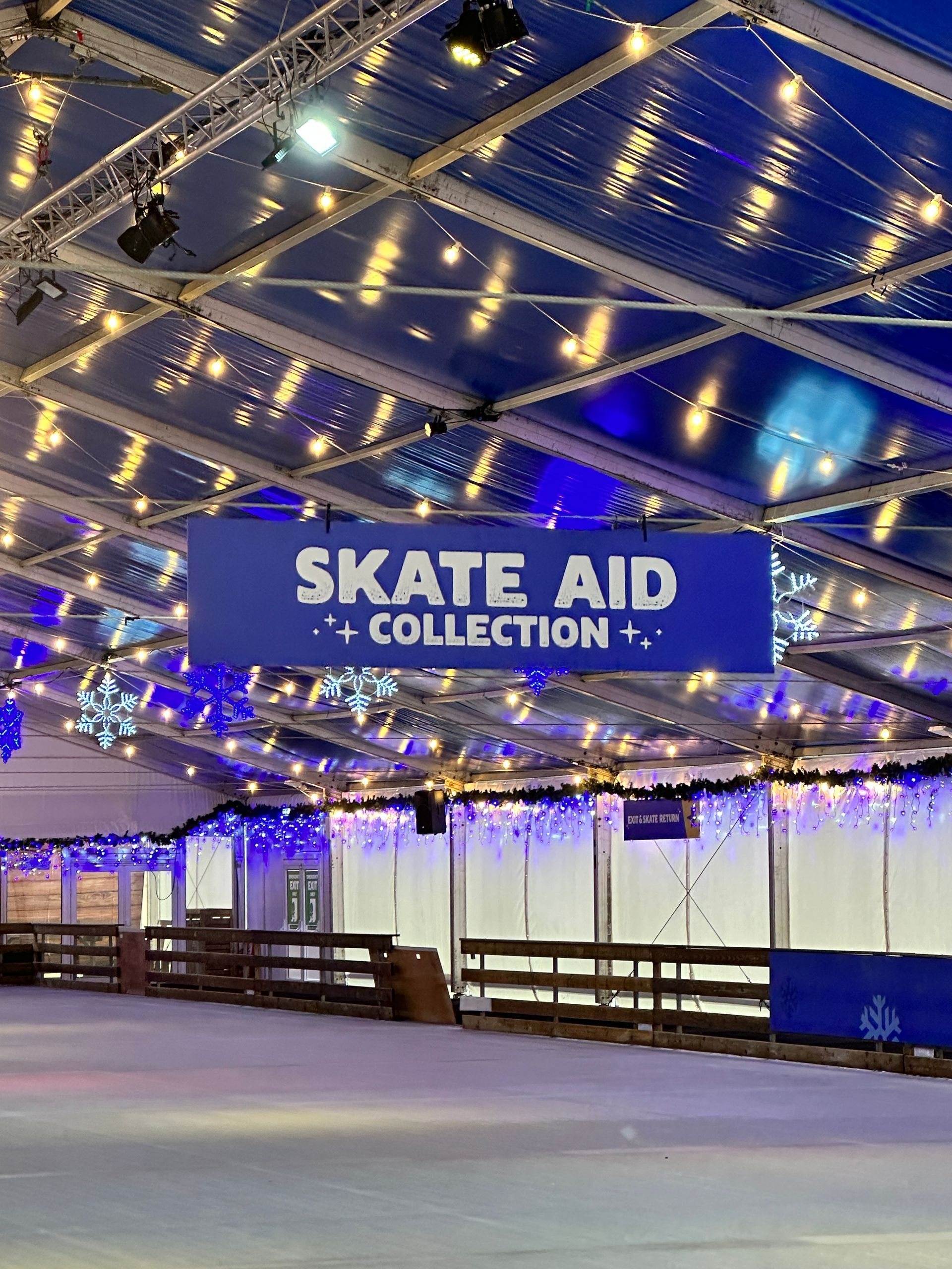 A skate aid collection sign hangs from the ceiling of an ice rink